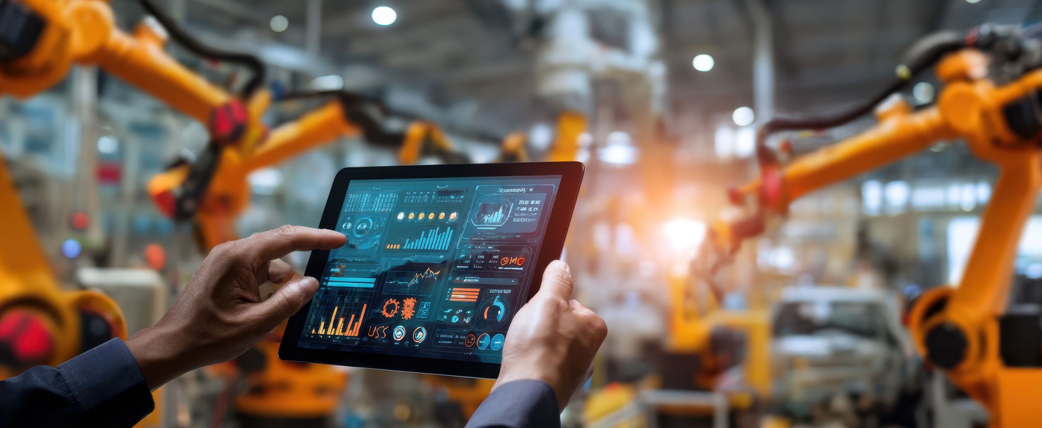 The tablet displaying analytics in an automated factory environment with robots.
