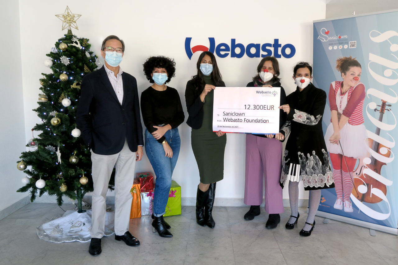 Webasto Foundation übergibt Spendenscheck über 12.300 EUR an Saniclown vor Weihnachtsbaum; Pressefoto zur Meldung über Webastos Engagement als Systempartner.