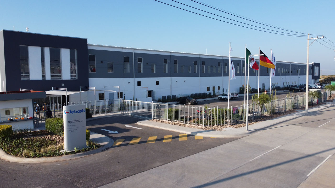 Außenansicht des neuen Webasto-Werks in Guanajuato, Mexiko, mit Einfahrt und Fahnen, unterstreicht die globale Standorterweiterung von Webasto als Systempartner.