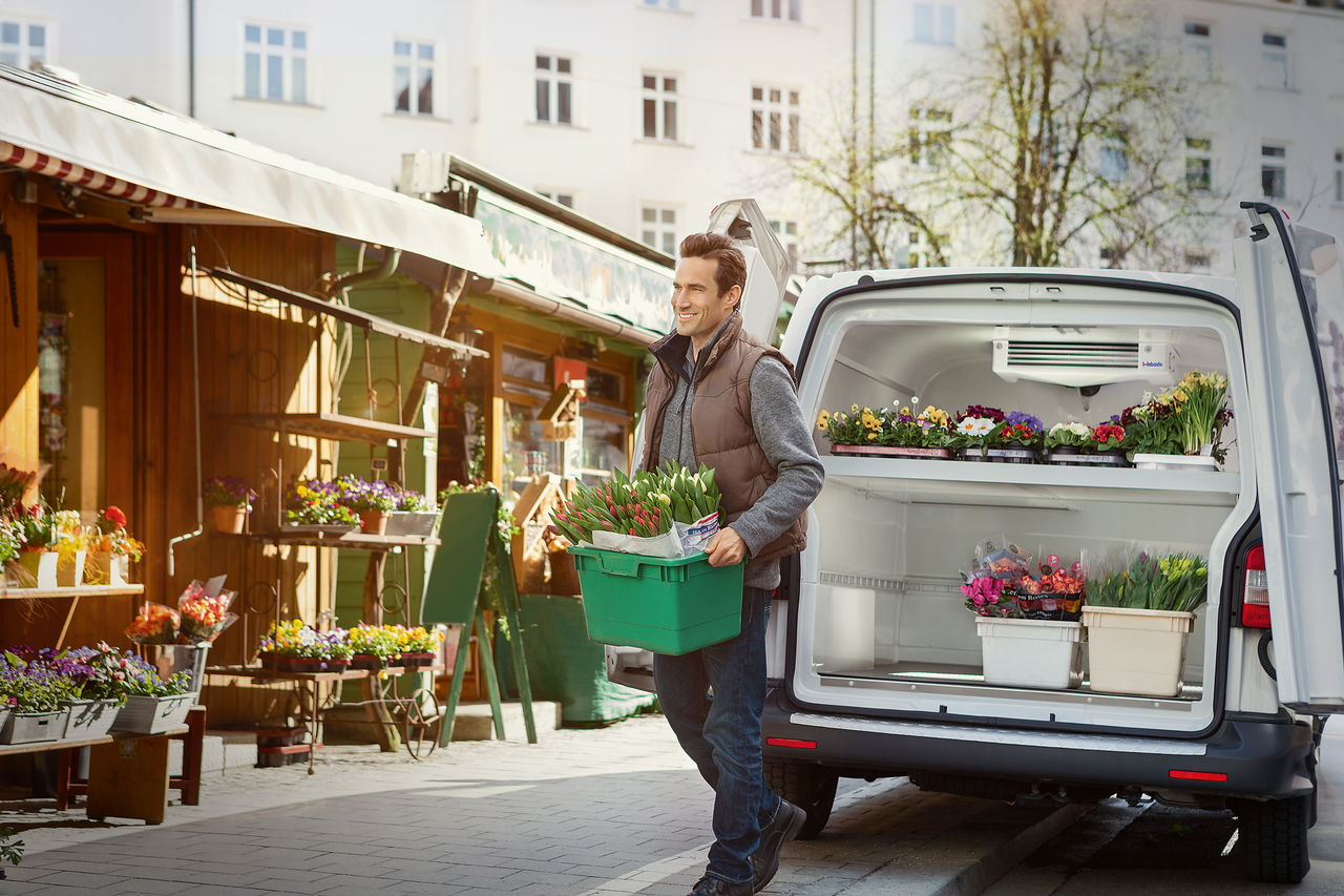 Vendor loads flowers from a temperature-controlled van with compact electric refrigeration, showcasing Webasto thermal management for perishable transport.