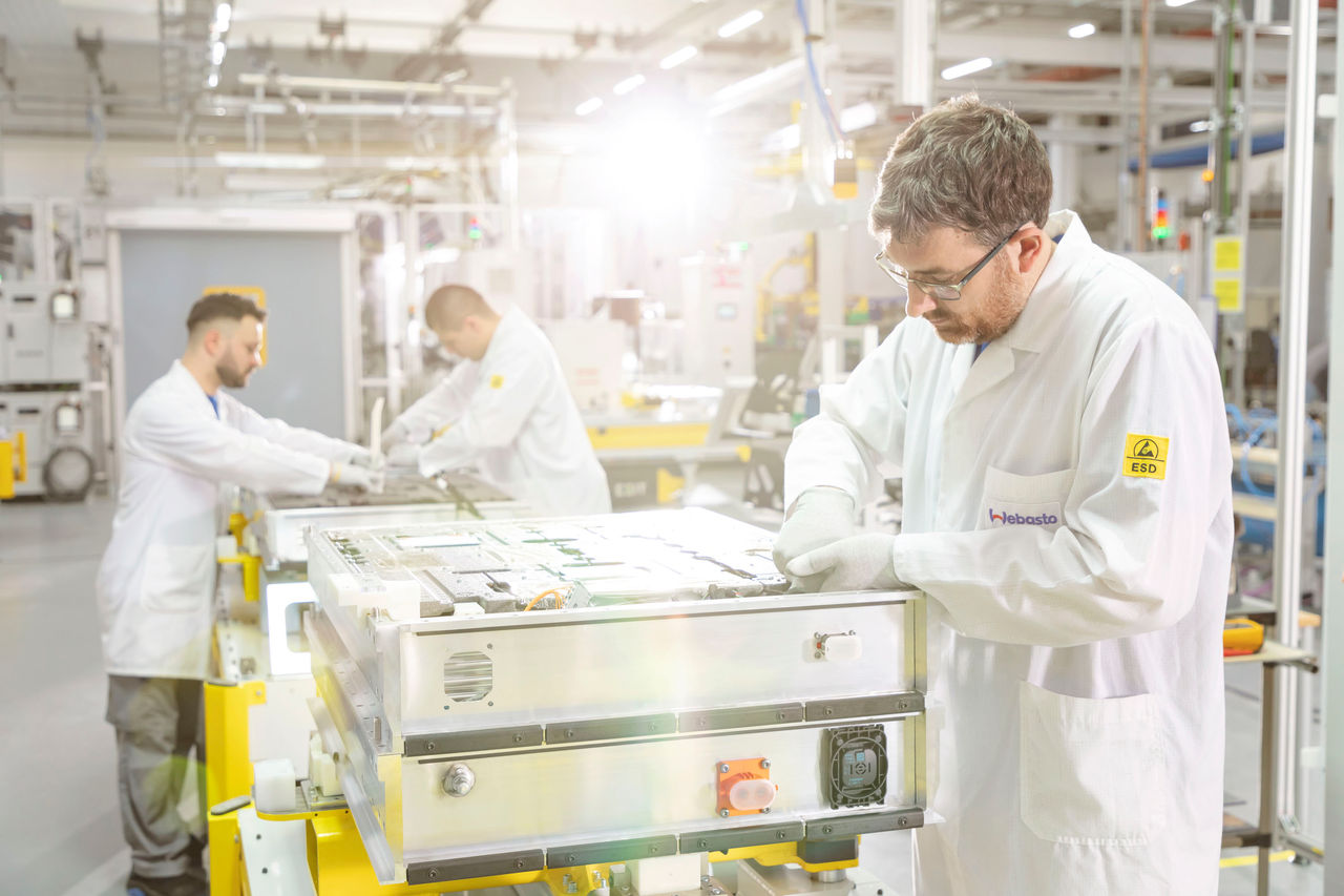 Technicians performing ESD-safe assembly and inspection of a high-voltage battery module on Webasto’s line, highlighting Webasto’s EV battery systems partnership.